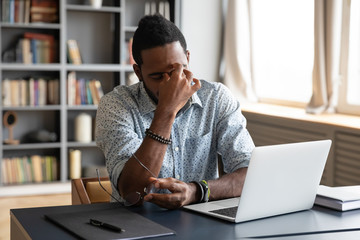 Frustrated young biracial guy taking off eyeglasses, massaging nose bridge, feeling tired due to computer overwork. Overwhelmed stressed millennial african american man suffering from eyes strain.