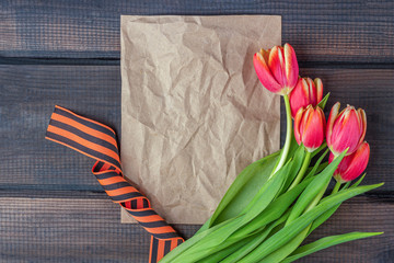 9 May background - template blank greeting card with red tulips, George ribbon and paper note on the wooden background. Victory day or fatherland defender day concept. Top view, copy space for text