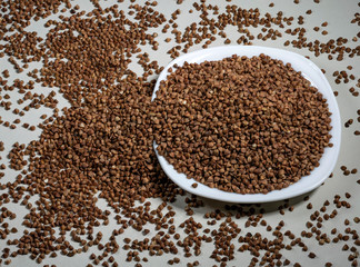 Raw buckwheat in a white plate on a gray background. Ingredient for cooking. View from above.