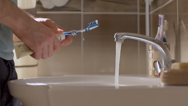 A young man brushes his teeth in a beautiful bathroom. Close up male hands squeezes the tooth paste onto the tooth brush and rinses his mouth with water. Daily Hygiene Procedures