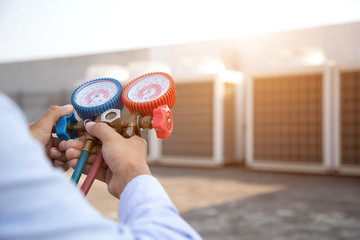 Technician using measuring equipment for filling air conditioners and checking outdoor air compressor unit.