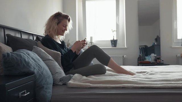 Young woman alone in bedroom texting and smiling