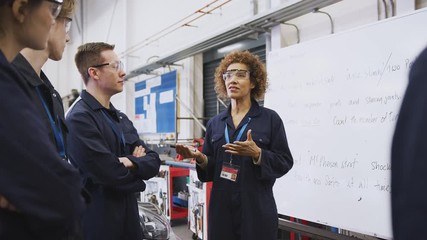 Female tutor by whiteboard with students teaching auto mechanic apprenticeship at college - shot in slow motion