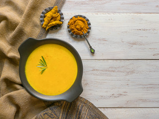 Healthy curcuma cream soup on white wooden background