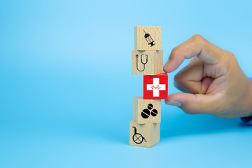 Close-up hand choose a cube wooden toy blocks with a red cross heart rhythm icon stacked for medical and health insurance concepts.