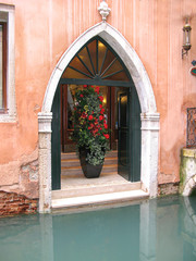 Fototapeta na wymiar Italy, Venice, the entrance to the hotel is arched. Entrance and stone steps to the canal. Pink wall and a huge bouquet of flowers in a vase.