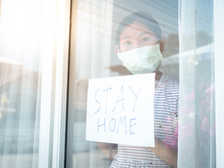 Asisan girl wearing mask holding paper message STAY HOME, during COVID-19.