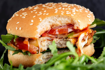 Bitten cheeseburger with a lot of arugula and sauces