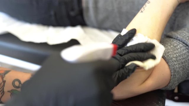 Female tattooist cleaning and refreshing the tattoo area with water.