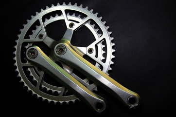 Detail for a road bike on a black background. Old school crankset and chainrings close-up. Soft side light with a slight yellow tint. Bicycle repair.