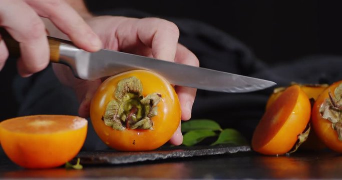 Male hand with a knife cut the persimmon in half.