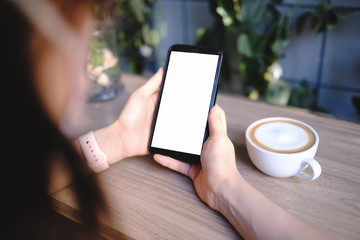 Mockup image of a woman holding and showing black mobile phone with blank screen in cafe