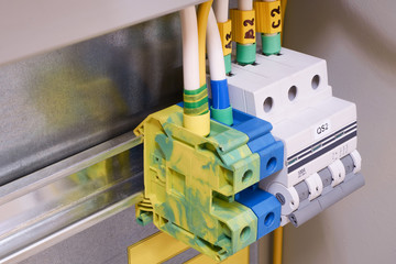 The electrical ground and neutral pass-through terminals and the circuit breaker are mounted on a rail in the electrical Cabinet. The ground terminal is yellow-green. The neutral terminal is blue.