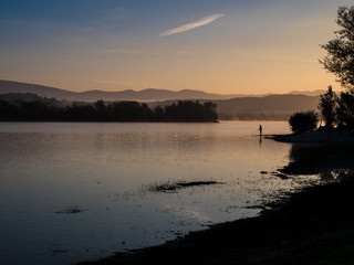 Fototapeta na wymiar Lonely fisherman angling at a lake in the early morning just after sunrise, Ullibarri-Gamboa Reservoir, Alava, Basque Country, Spain