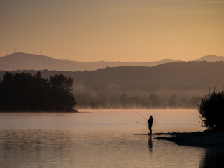Lonely fisherman angling at a lake in the early morning just after sunrise, Ullibarri-Gamboa Reservoir, Alava, Basque Country, Spain