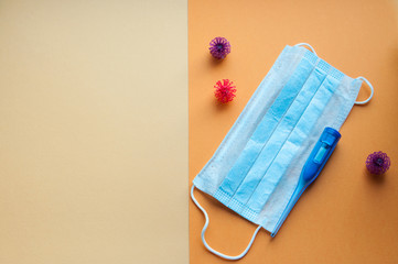 Protective face mask and  thermometer  on orange background. Concept of coronavirus pandemic. Virus and COVID-19 self protection.