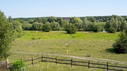Countryside summer landscape and young boy running with colourful flying kite in green sunny field on summer day in village. Happy summer travel, vacations and fun concept.