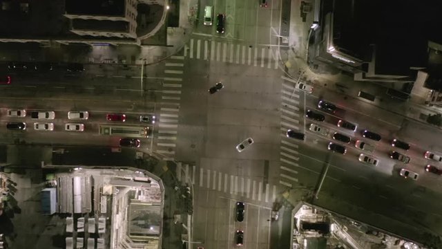 AERIAL: Overhead Rising on Intersection Street with big Construction Site and Holes in Ground at Night with Glowing Streets and City Car Traffic Lights 
