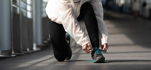 Young sports woman tying shoe lace in the city.