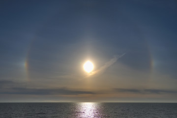 Rainbow glow around the sun in a haze above the sea. Halo - a sign of worsening weather