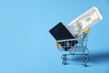 Dollar bills and credit cards in shopping cart on shopping isolated on a blue background. close-up of shopping trolley. Purchasing power and living wage concept with copy space.