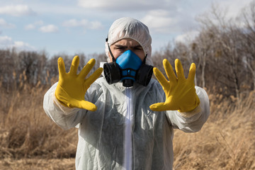 A man in a chemical protective suit and a respirator in the open air shows a stop sign with both hands. Air pollution. Concept of the Chinese pandemic coronavirus.