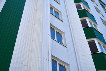 facade of a new multistory building with white and green metal siding, many Windows