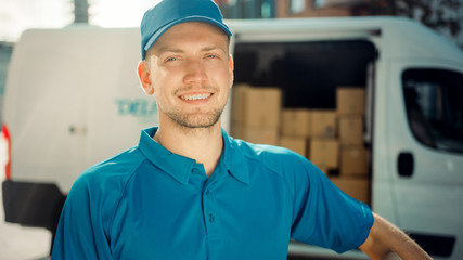 Portrait of Handsome Delivery Man Holds Cardboard Box Package Standing in Modern Stylish Business District with Delivery Van in Background. Smiling Courier On Way to Deliver Postal Parcel to Client