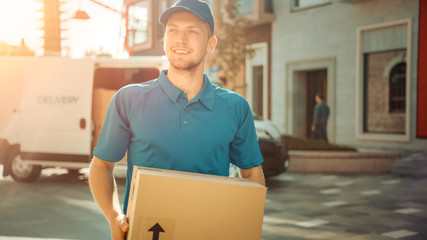 Portrait of Delivery Man Holds Cardboard Box Package Standing in Modern Stylish Business District with Delivery Van in Background. Smiling Courier On Way to Deliver Postal Parcel to Client. Sun Flare - obrazy, fototapety, plakaty