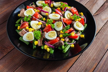 healthy tuna salad with boiled egg corn tomato red onion parsley green bean on black plate