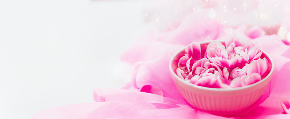 Aroma water bowl with pink flowers at light silk background. Spa and wellness composition. Banner. Essential water .