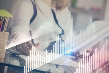 A woman hands writing information about stock market in notepad. Forex chart holograms in front. Concept of research.