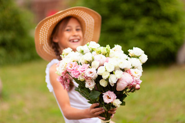 Obraz premium A smiling girl holds a beautiful bouquet of pink and white peonies in her hands. A child in a straw hat. Sunny summer day.