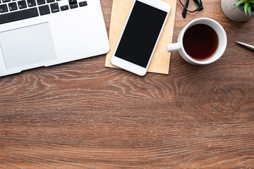 Wood office desk table with smartphone with blank screen, laptop computer, cup of coffee and...