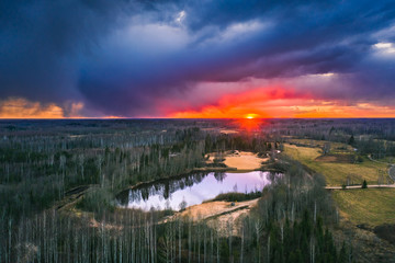 Obraz premium Aerial view over forest with dark storm clouds. Lake in the forest at colorful twilight. 