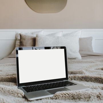 Blank screen laptop on bed with pillows in front of beige wall. Copy space mockup template. Work at home concept for social media, website, blog.