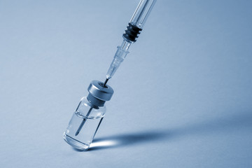 Syringe needle pierces the cap of medical vial. Monochrome photo close-up.