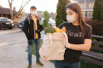 Courier in protective mask and medical gloves delivers fresh food for female customer. Delivery service under quarantine. Coronavirus covid-19 theme