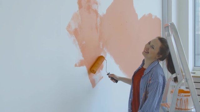 Singleton lifestyle concept. Young happy woman paints her walls orange with a roller