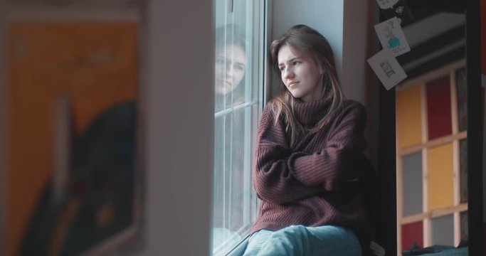 The girl has a stomach ache. Girl sitting on a windowsill near the window. Camera - Canon 5D Mark IV