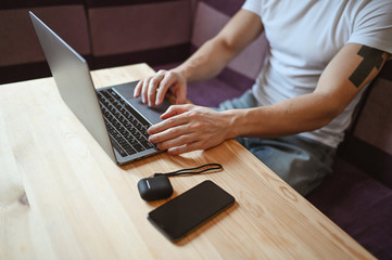 Unrecognizable man hands with smartphone and headphones working on a laptop during coronavirus isolation home quarantine. Covid-19 pandemic Corona virus. Distance online work from home concept.