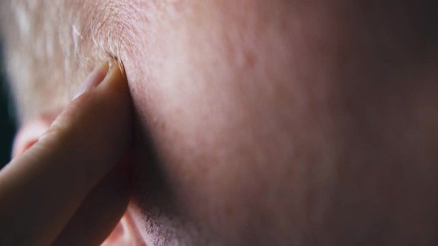 CU: person massages cheekbone with fingers near grey hair and ear under electric light extreme close view