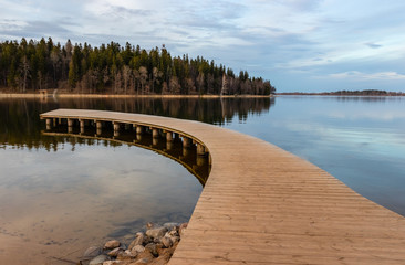A wooden footbridge on the lake, also used as a summer boat dock. The forest behind the lake, reflections in the calm water.Environmental improvement. Latvia. Aluksne.