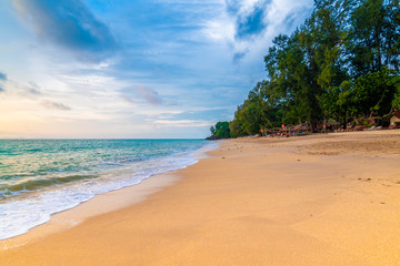 View of tropical beach at Koh Lanta island, Thailand. Bar on the beach are prepared for tourist during beautiful sunset. Soft light, vibrant colors. Sky with clouds above tranquil sea.