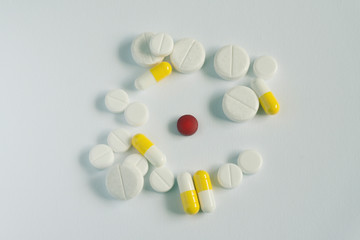 one red and many white pills on white background