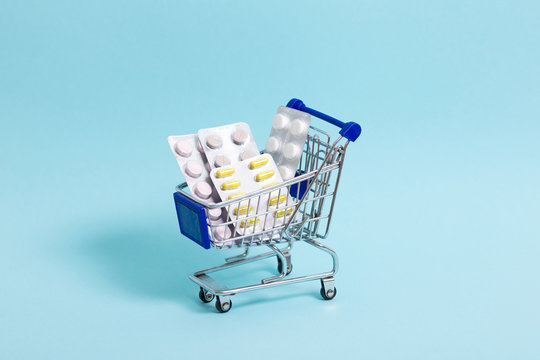 blue shopping cart with pills stands on a blue background close-up. Concept of healthcare, online shopping, high cost of medicines. Copy space