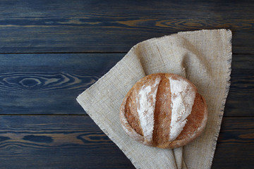 Round loaf of freshly bread with a linen napkin on a dark wooden background.