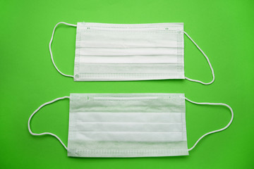 Two medical face masks isolated on a green background.