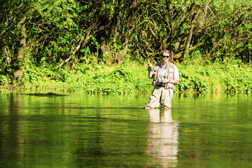 Fly fishing on the river in a rural place in the summer, young fishing woman standing in the water