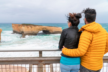 Couple & Rock formations with ocean sea waves on coastline. London Arch gorge on Great Ocean Road, Melbourne, Australia. Road trip to Australian. Sand, sea, holiday, vacation. Twelve Apostles